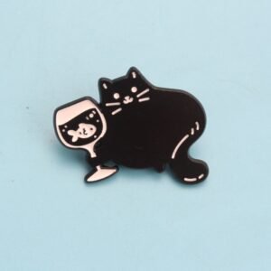 Enamel pin of a black cat holding a wine glass that contains a small white fish.