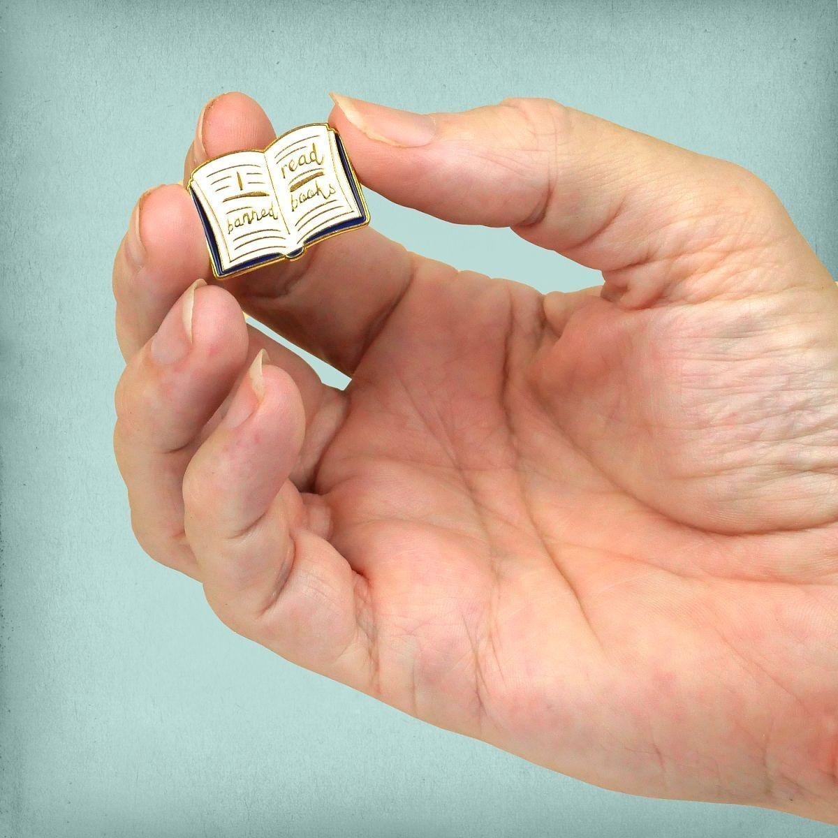 Book worm gift idea pin held to show the small, detailed craftsmanship of the enamel.