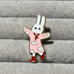 A white bunny character enamel pin wearing a pink dress with white spots, a red neckerchief, and red boots.