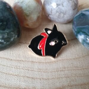 Small black bunny enamel pin with a red ribbon and pink ears, resting on a wooden surface.