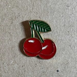 Enamel pin of two bright red cherries attached to a green stem with a single leaf.