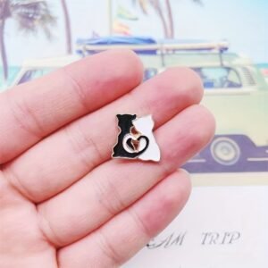 Hugging cats enamel pin held between fingers to show scale.