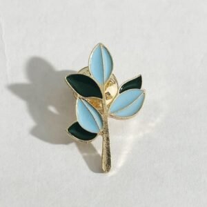 Gold-toned enamel pin shaped like a small branch with two shades of blue leaves.