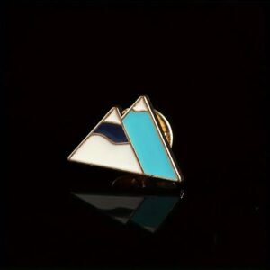 Mountain enamel pin with turquoise and navy details in a gold metal frame.