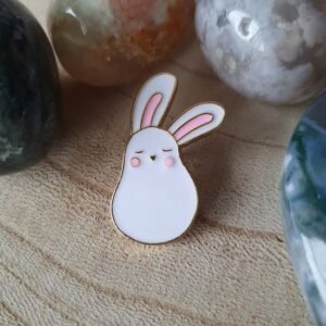 A white pear-shaped bunny enamel pin with pink ears and cheeks, shown with closed, sleepy eyes.