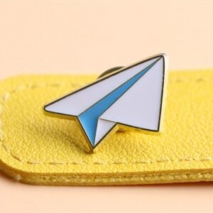 A high-quality paper plane enamel pin featuring a clean white and light blue geometric design.