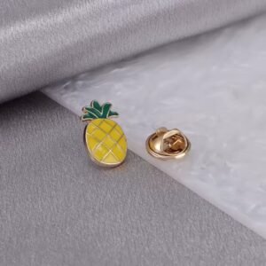 Pineapple enamel pin with yellow and green enamel and gold finish on a grey surface.