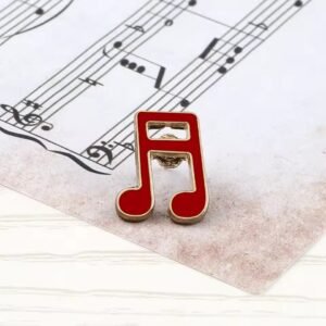 Music enamel pin in red and gold resting on sheet music.