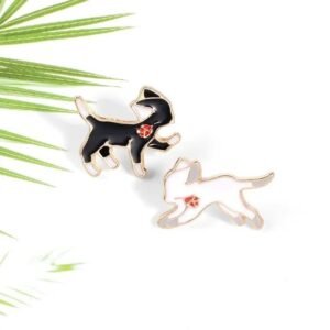 Two separate enamel pins of running cats, one black and one white, both featuring a red heart on their hip and gold outlines.