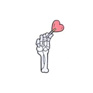 White skeleton hand enamel pin holding a pink heart-shaped lollipop.