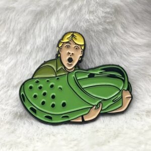 Enamel pin showing a surprised blonde man holding a massive green foam clog shoe.