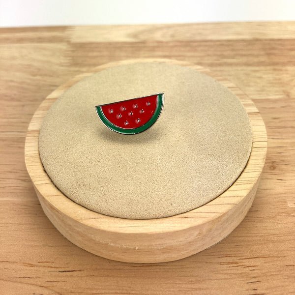 Watermelon slice enamel pin displayed on a neutral accessory holder.