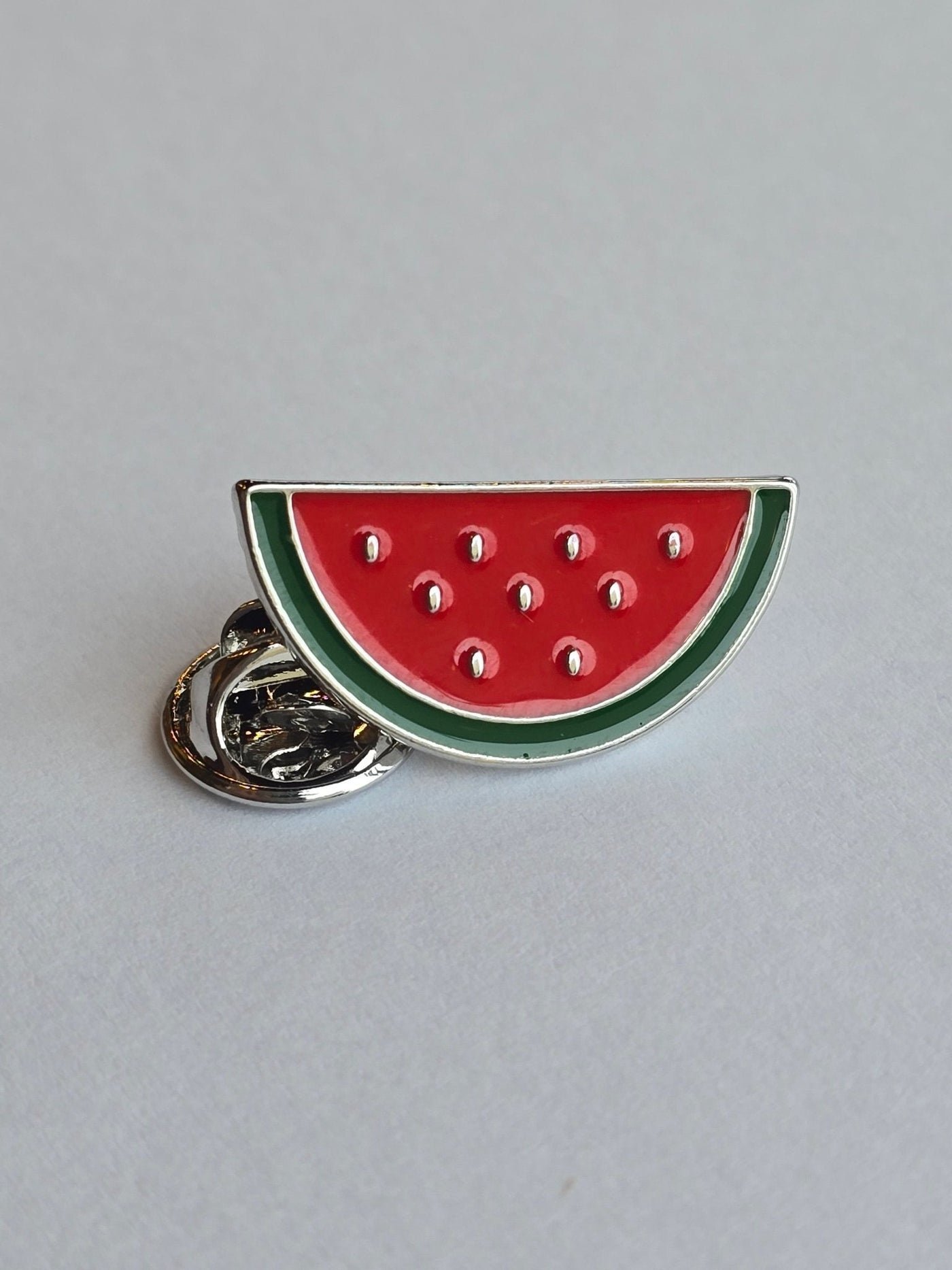 Watermelon slice enamel pin featuring vibrant red and green enamel with a silver butterfly clutch.