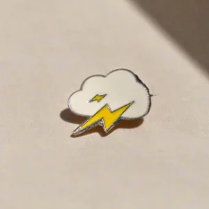 Aesthetic white storm cloud enamel pin with two bright yellow lightning bolts and polished gold-toned edges.