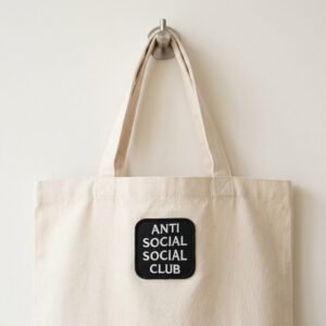 Anti Social patch on a natural canvas tote bag hanging on a hook