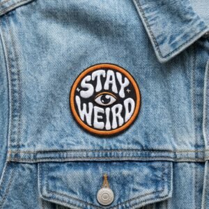 Toppa “Stay Weird” con disegno di un occhio su una giacca di jeans azzurra
